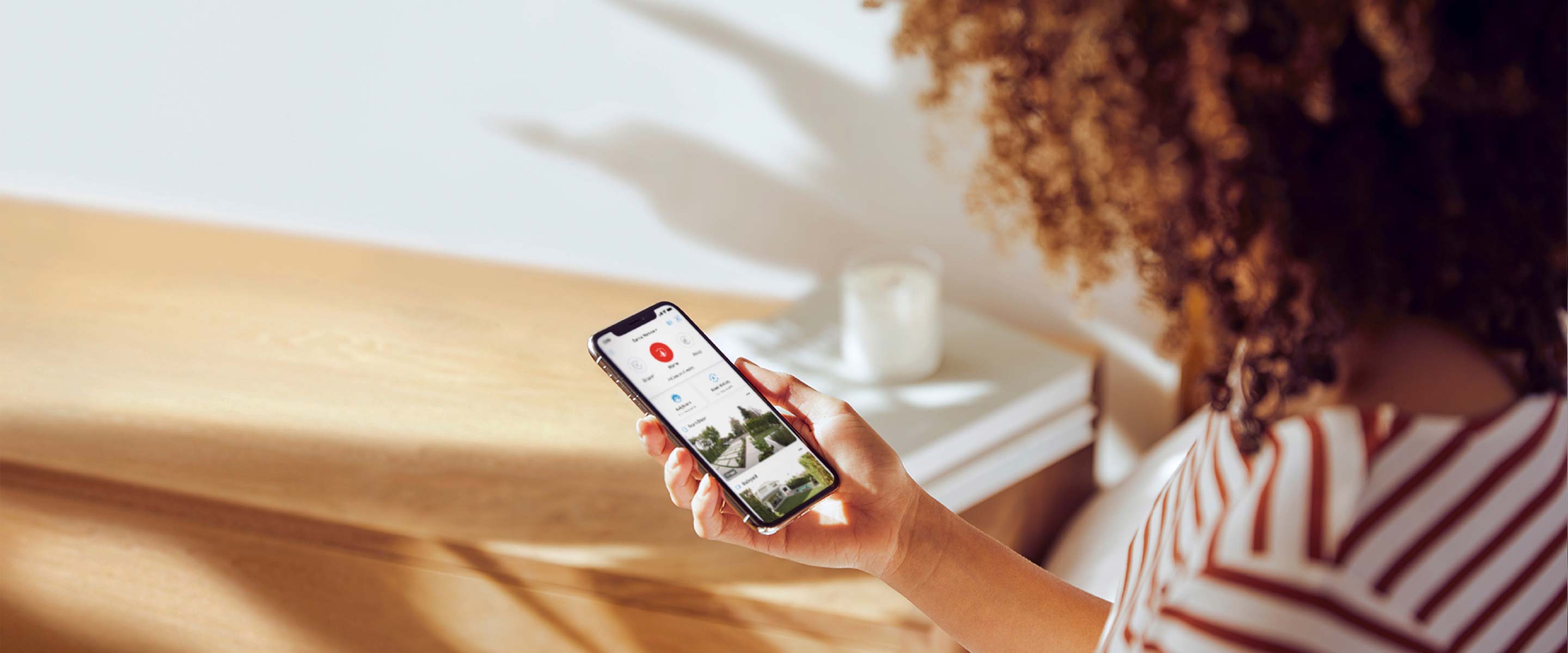 Woman holding a smartphone displaying the Rivergrove App, monitorartoria her home security feed in a well-lit room.